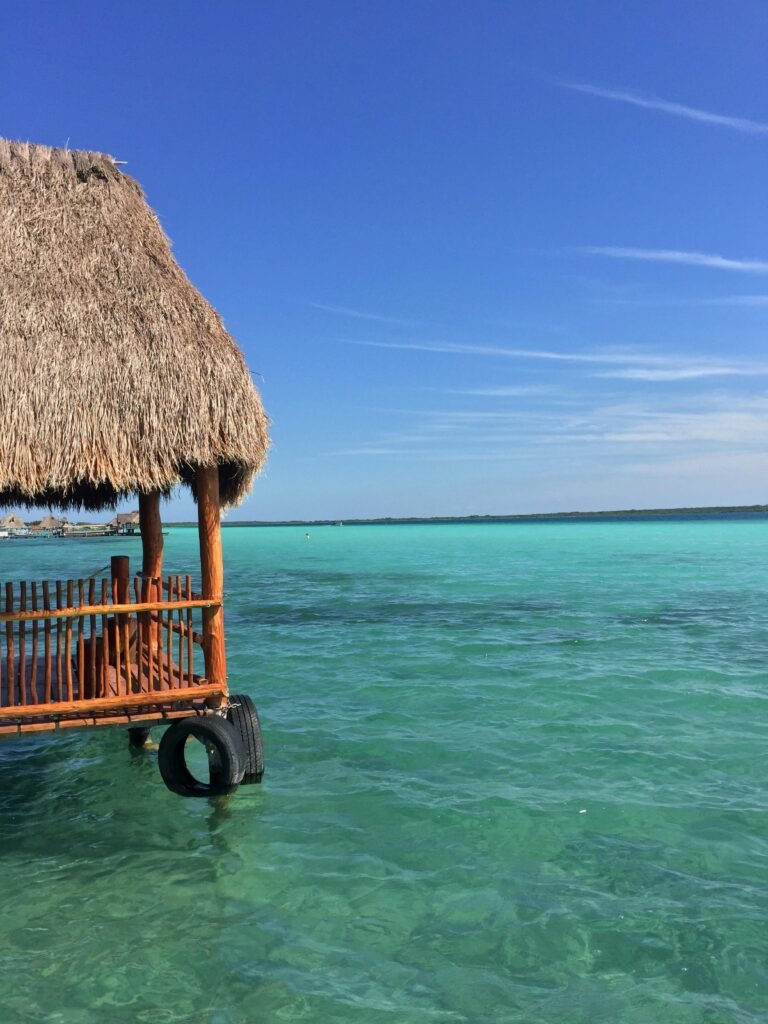 A picturesque view of Bacalar Lagoon in Mexico with a traditional thatched hut overlooking turquoise waters under a clear blue sky.