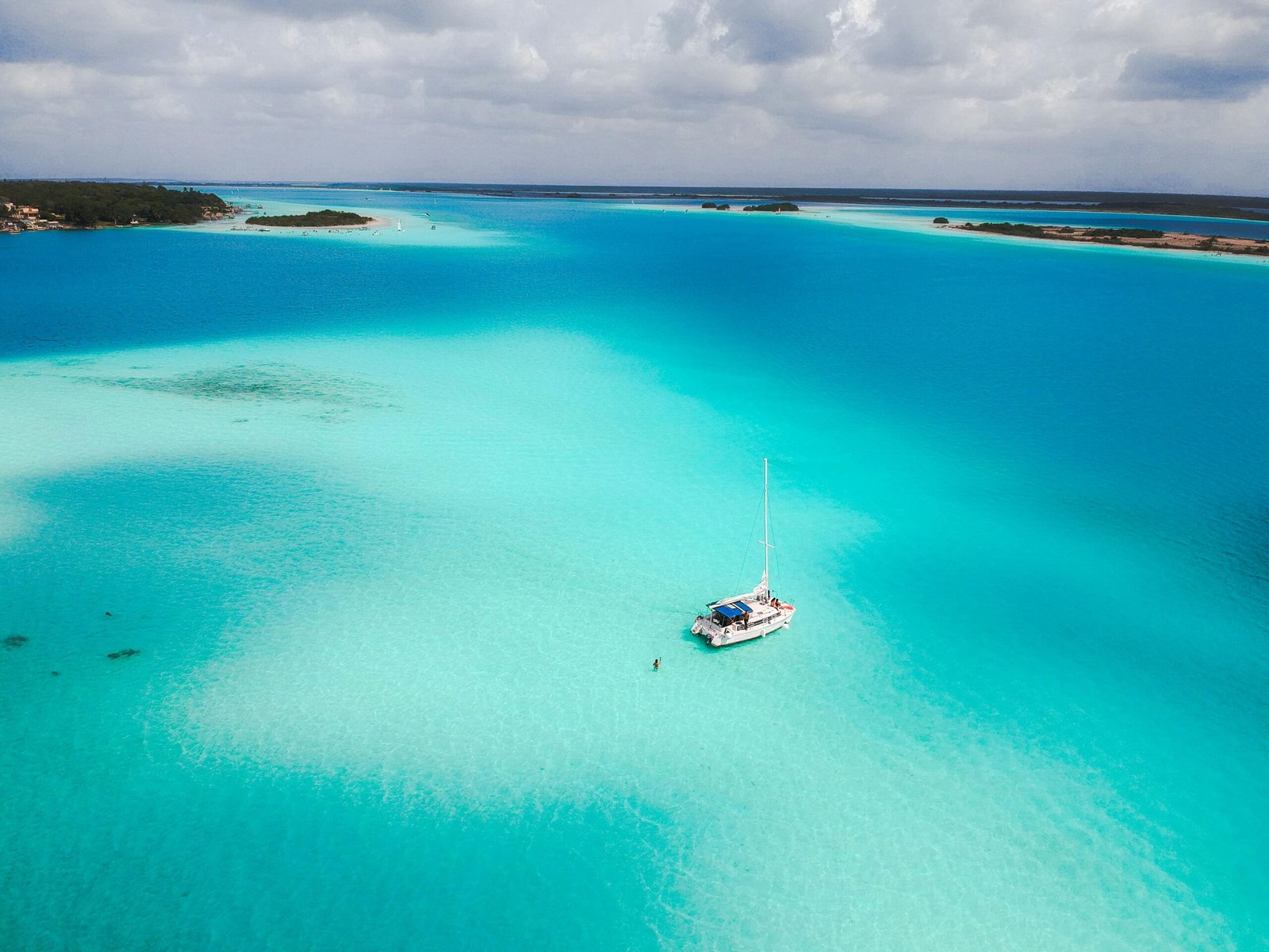 A stunning aerial view of a sailboat in the tranquil turquoise waters of Bacalar Lagoon, Mexico.